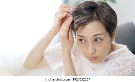 Middle aged Asian woman worrying about her hair. Beauty concept. Thinning hair. Hair care.
