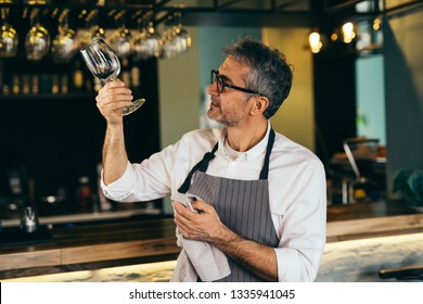 Middle aged barman polishing the wine glass in cafe bar - Powered by Shutterstock