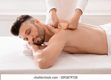 Middle aged bearded man attending modern male spa, laying on massage table, getting healing body procedure, enjoying his day at spa. Masseuse pressing on man back, using acupressure technique