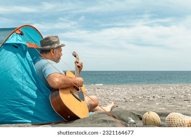Middle aged bearded man playing guitar and singing while camping picnic on the beach in summer vacation. - Powered by Shutterstock