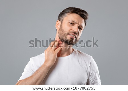 Middle aged bearded man scratching highlighted with red neck on grey studio background, copy space. Annoyed man suffering from itch, having rash on his neck. Allergic reaction, eczema concept