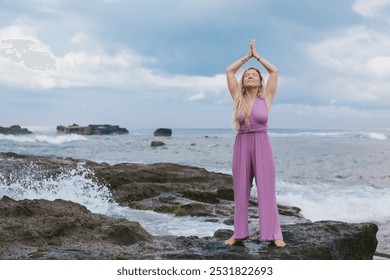 Middle aged beautiful white woman with blonde hair practicing yoga, spirituality, yoga retreat, asana and meditation, lilac jumpsuit, outdoor, rocky beach, waves, splashes, energy, praying hands - Powered by Shutterstock