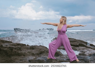 Middle aged beautiful white woman with blonde hair practicing yoga, spirituality, yoga retreat, asana and meditation, lilac jumpsuit, outdoor, rocky beach, waves, splashes, energy, praying hands - Powered by Shutterstock