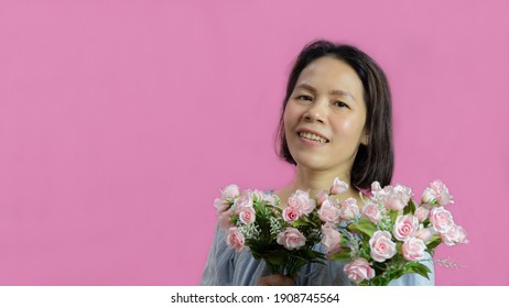 Middle Aged Black Haired Asian Woman Holding A Bouquet Of Pink Roses Is Smiling Happily Receiving Flowers On The Theme Of Valentine's Day Portrait Of A Young Woman On A Pink Background.