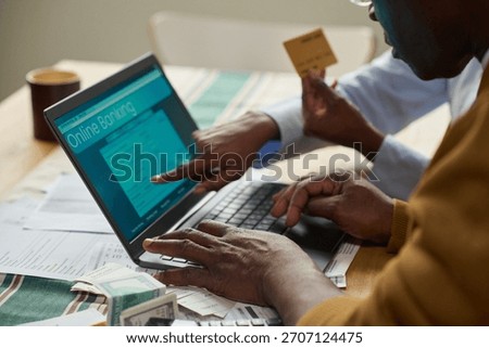 Middle aged Black man using laptop for online tax payment while middle aged Black woman holding credit card and pointing at computer screen, tax documents and cash on table