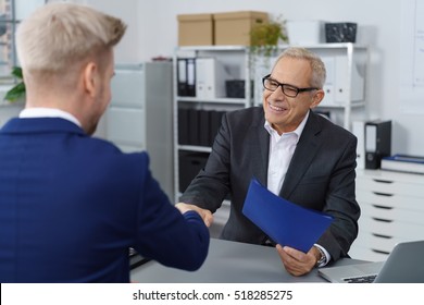 Middle Aged Boss In Eyeglasses And Dark Suit Shaking Hands With Young Job Seeker In Blue