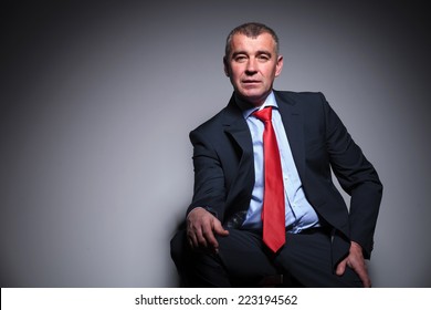 Middle Aged Business Man Sitting On A Stool, Resting His Hand On His Knee While Looking At The Camera.