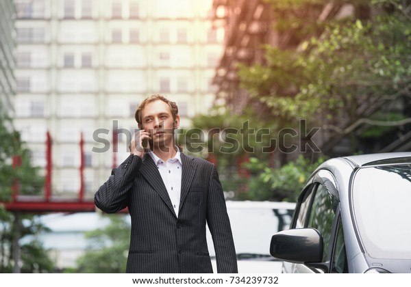 Middle aged businessman calling with smart phone\
beside of a car.