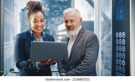 Middle Aged Businessman Talking with International Investment Partner while Riding Glass Elevator to Office in a Modern Business Center. Corporate Associates Use Laptop Computer in a Lift. - Powered by Shutterstock