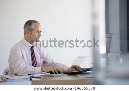 Middle aged businessman using computer at office desk