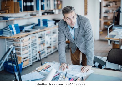 Middle aged Caucasian architect working on building plans in a modern company office - Powered by Shutterstock