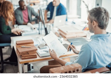 Middle aged Caucasian architect working on building plans in a modern company office - Powered by Shutterstock