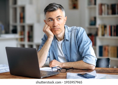 Middle aged caucasian business man or freelancer sitting at workplace, working on laptop, resting head on hand because of tired, doing work overtime, stressed and bored, need rest, pensive looks away - Powered by Shutterstock