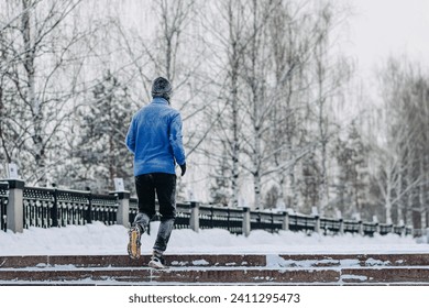 middle aged caucasian man runs up stairs in park in winter, blue jacket, black trousers and balaclava to protect face from cold, active lifestyle concept, jogging in winter, sport life, copy space