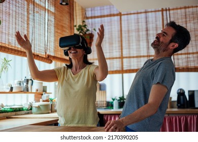 A Middle Aged Caucasian Woman Is Using An Augmented Reality Headset With Her Husband Next To Him Laughing At Her Being Goofy