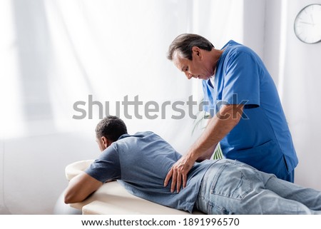 middle aged chiropractor working with young and injured african american patient on massage table in clinic