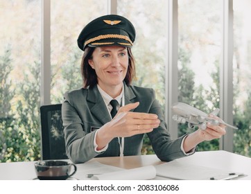 Middle Aged Commercial Female Pilot Holds Aircraft Model Smiling Face Explaining. Beautiful Mature Woman Airplane Captain Flight Instructor Has Meeting Discussion With Team. Aviation Business Concept.