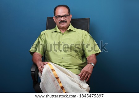 Middle aged confident man wearing traditional Kerala dress sitting on a chair 