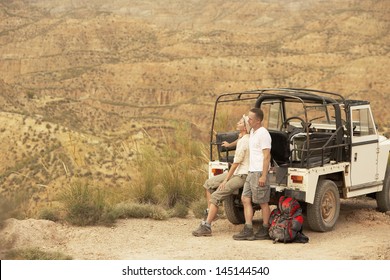 Middle Aged Couple In Back Of Four-wheel-drive Car On Cliff Edge In Desert