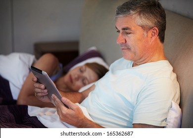 Middle Aged Couple In Bed With Man Using Tablet Computer - Powered by Shutterstock