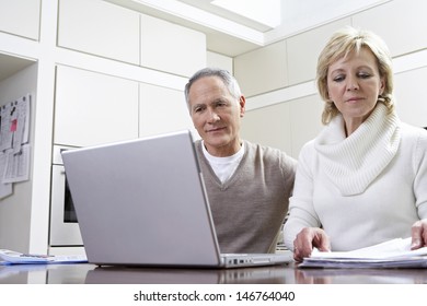 Middle Aged Couple Calculating Home Finances On Laptop At Kitchen Table