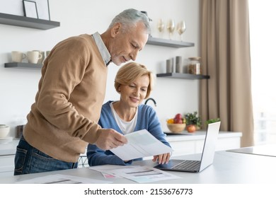 Middle aged couple checking finance account together. Wife and husband fill tax form, holding current expense document in hands, sitting on kitchen, paying utility bill online - Shutterstock ID 2153676773