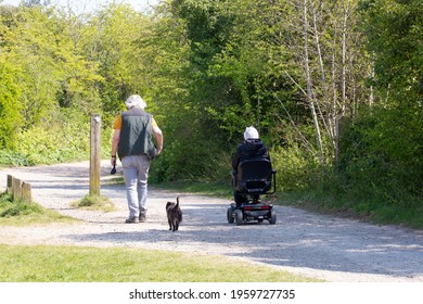 A Middle Aged Couple In The Countryside Walking The Dog With The Lady Using A Mobility Scooter