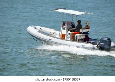 Middle Aged Couple Leisurely Cruising Biscayne Bay Near Miami Beach In A Pontoon Fishing Boat With Canopied Center Console Powered By A Single Outboard Engine.