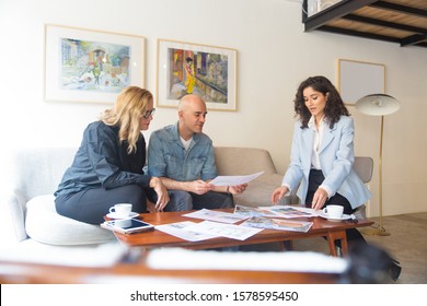 Middle Aged Couple Meeting With Interior Designer To Discuss Renovation Project. Man And Women Sitting In Living Room At Home And Talking. Designer Occupation Concept