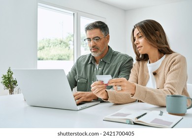 Middle aged couple older senior mature man and woman using laptop looking at computer holding credit card buying online, making banking payments during ecommerce shopping sitting at home table. - Powered by Shutterstock