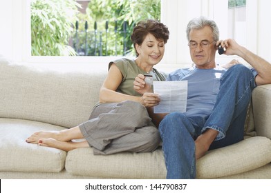Middle aged couple paying bill by phone on couch at home
