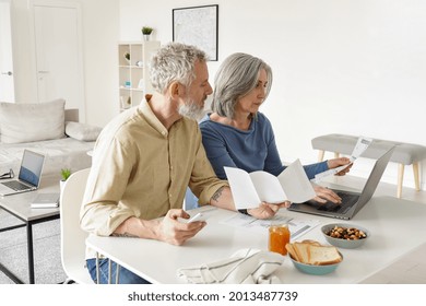 Middle Aged Couple Paying Financial Bills Online Using Computer At Home. Older Mature Husband And Wife Checking Bank Documents, Reading Papers, Calculating Taxes, Planning Retirement Pension.