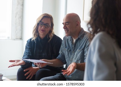 Middle Aged Couple Reading Document And Shrugging. Man And Women Sitting In Living Room At Home And Talking. Paperwork Concept