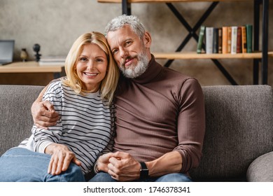 Middle Aged Couple Relaxing On Couch Smiling At Camera At Home In Living Room