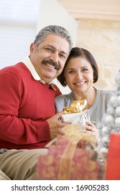 Middle Aged Couple Sitting On Sofa Holding Christmas Present