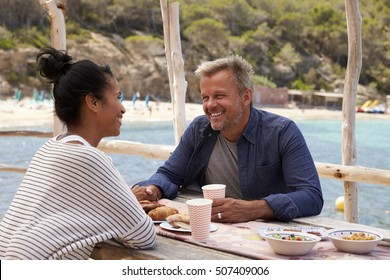 Middle Aged Couple Smiling Across A Table By The Sea, Ibiza