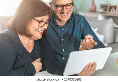 Middle Aged Couple Smiling While Shopping Online - Seniors Chat With Friends And Family - Warm Filter On Background - Focus On The Man