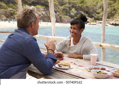 Middle Aged Couple At Table By The Sea Looking At Each Other