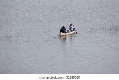 A Middle Aged Couple And Their Dog Canoeing Across A Lake.