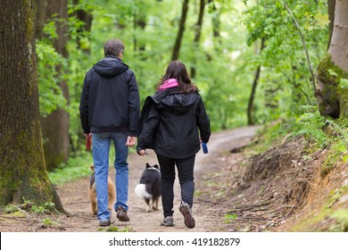 Middle Aged Couple Walking Their Two Dogs In Forest.