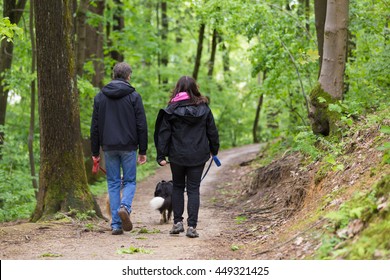 Middle Aged Couple Walking Their Two Dogs In Forest.