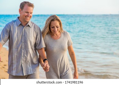 Middle Aged Couple Walking Together Holding Hands On The Beach. Sharing A Loving Moment Together While On A Tropical Vacation