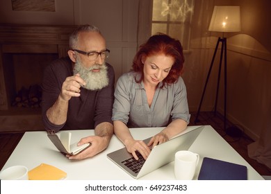 Middle Aged Couple Working On Laptop While Sitting At Table