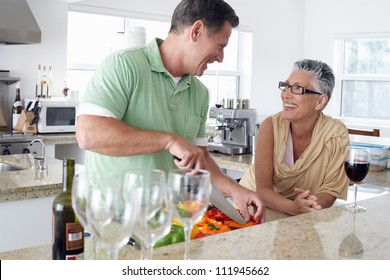 Middle aged cutting vegetables at kitchen counter with woman standing aside