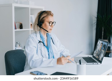 middle aged doctor in white coat and video conferencing headset make online video call consult patient on laptop. Telemedicine concept for domestic health treatment. Online remote medical appointment. - Powered by Shutterstock