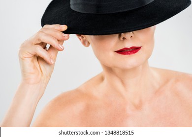 Middle Aged Elegant And Fashionable Woman With Red Lips Touching Black Hat Isolated On Grey 