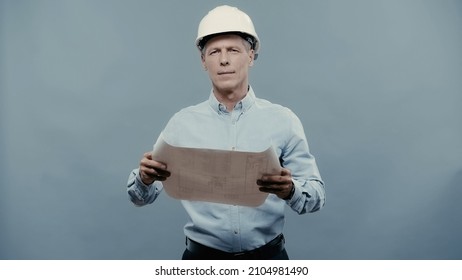 Middle aged engineer in hardhat holding blueprint and looking at camera isolated on grey