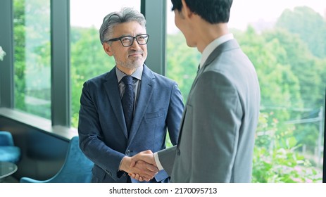 Middle Aged Executive Man And Young Businessperson Shaking Hands In The Office.