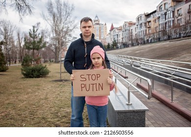 Middle aged father with his daughter holding a poster with anti-war message over cityscape background. Protest against the Russian intervention to Ukraine, activism and human rights movement