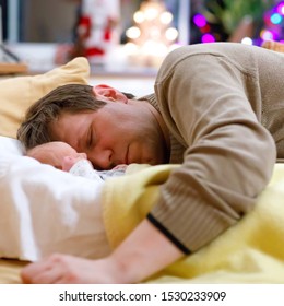 Middle Aged Father Sleeping Near His Newborn Baby Daughter On Christmas. Young Dad Cuddling With Baby Girl At Home. Happy Parenthood, Carefree Childhood, Family, Love. Cute Adorable Baby Sleeping.